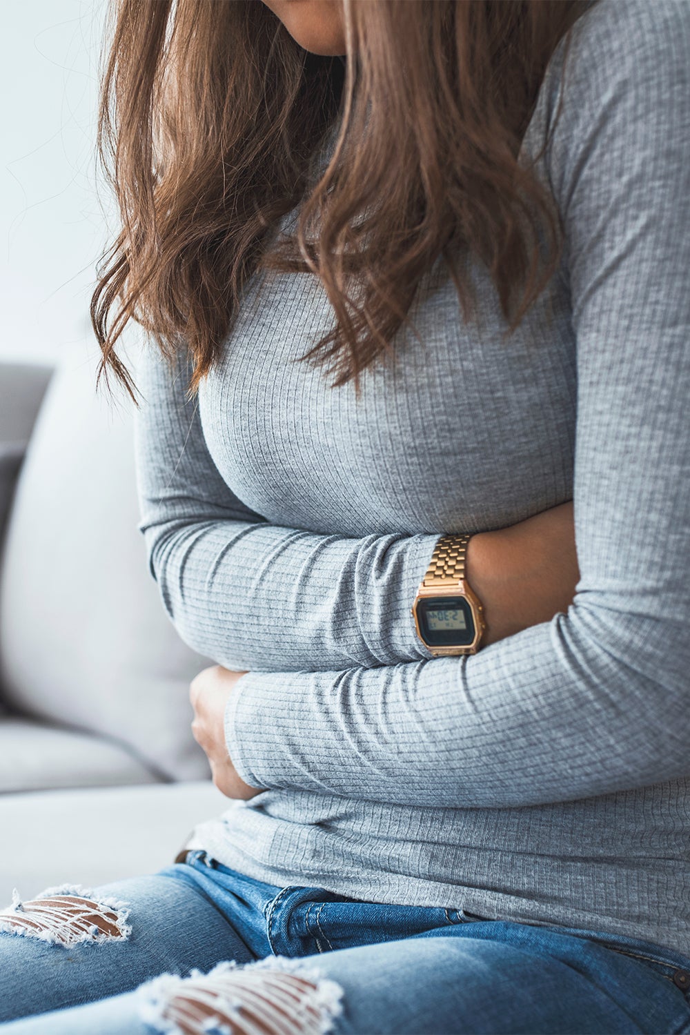 Woman lying on sofa looking sick in the living room. Young woman lying on bed and holding hands on her stomach. Woman having painful stomachache on bed, Menstrual period