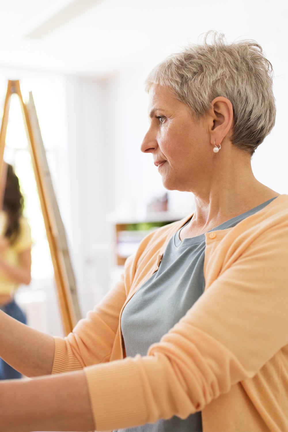 happy senior woman artist with easel and pencil drawing picture at studio